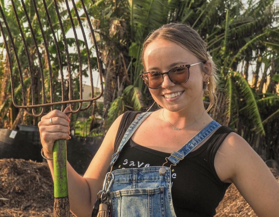 person standing with a pitchfork in front of compost area 